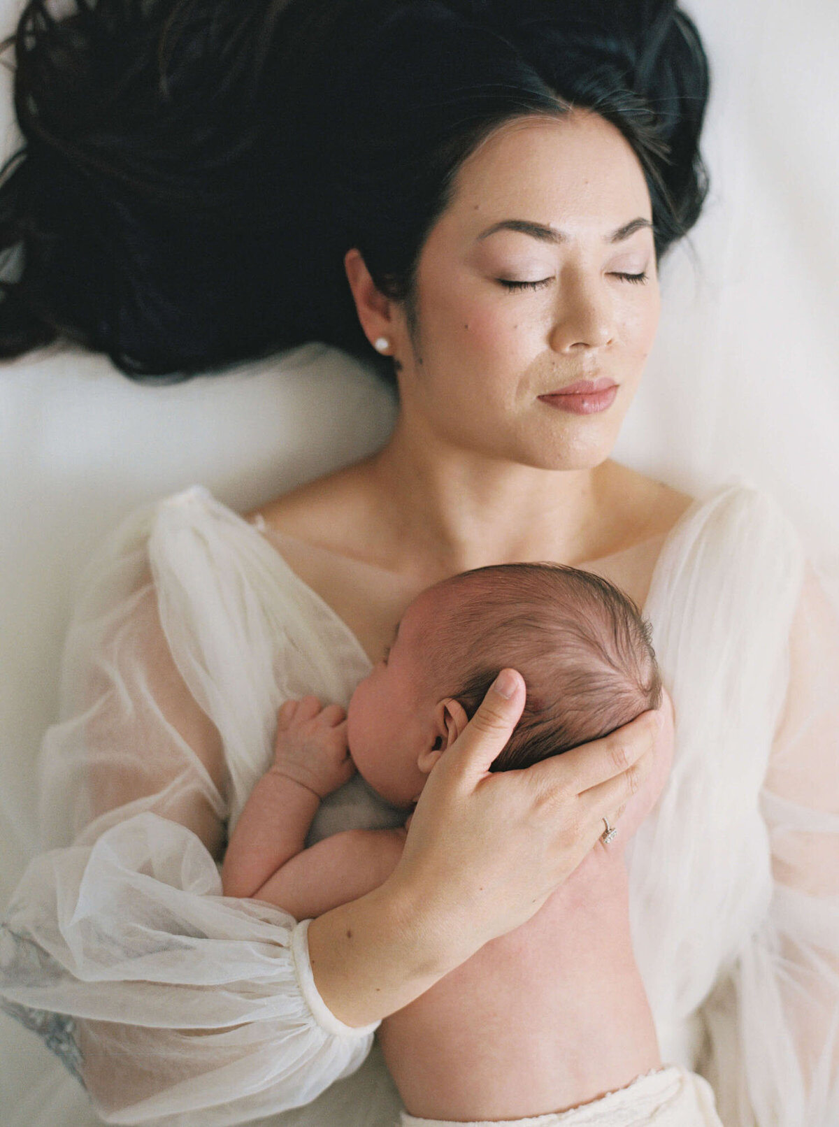 Mother laying on bed for newborn photos with Bay Area newborn photographer session.