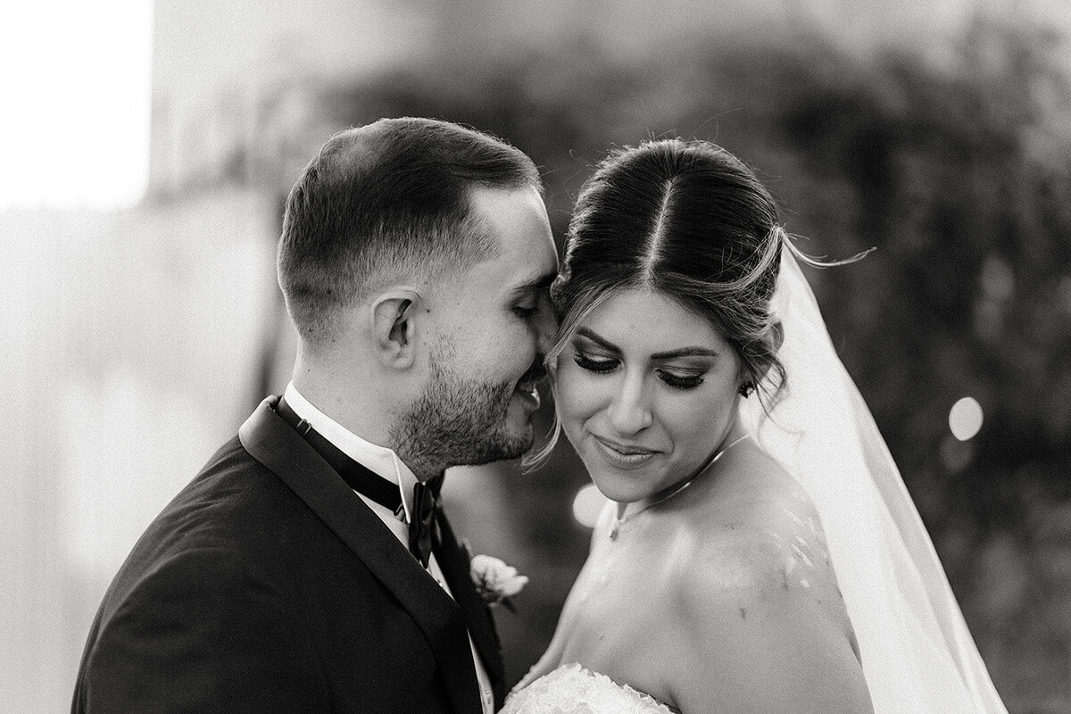In a close-up, the groom leans in towards his bride, who gazes down softly, both savoring a peaceful moment together in black-and-white.