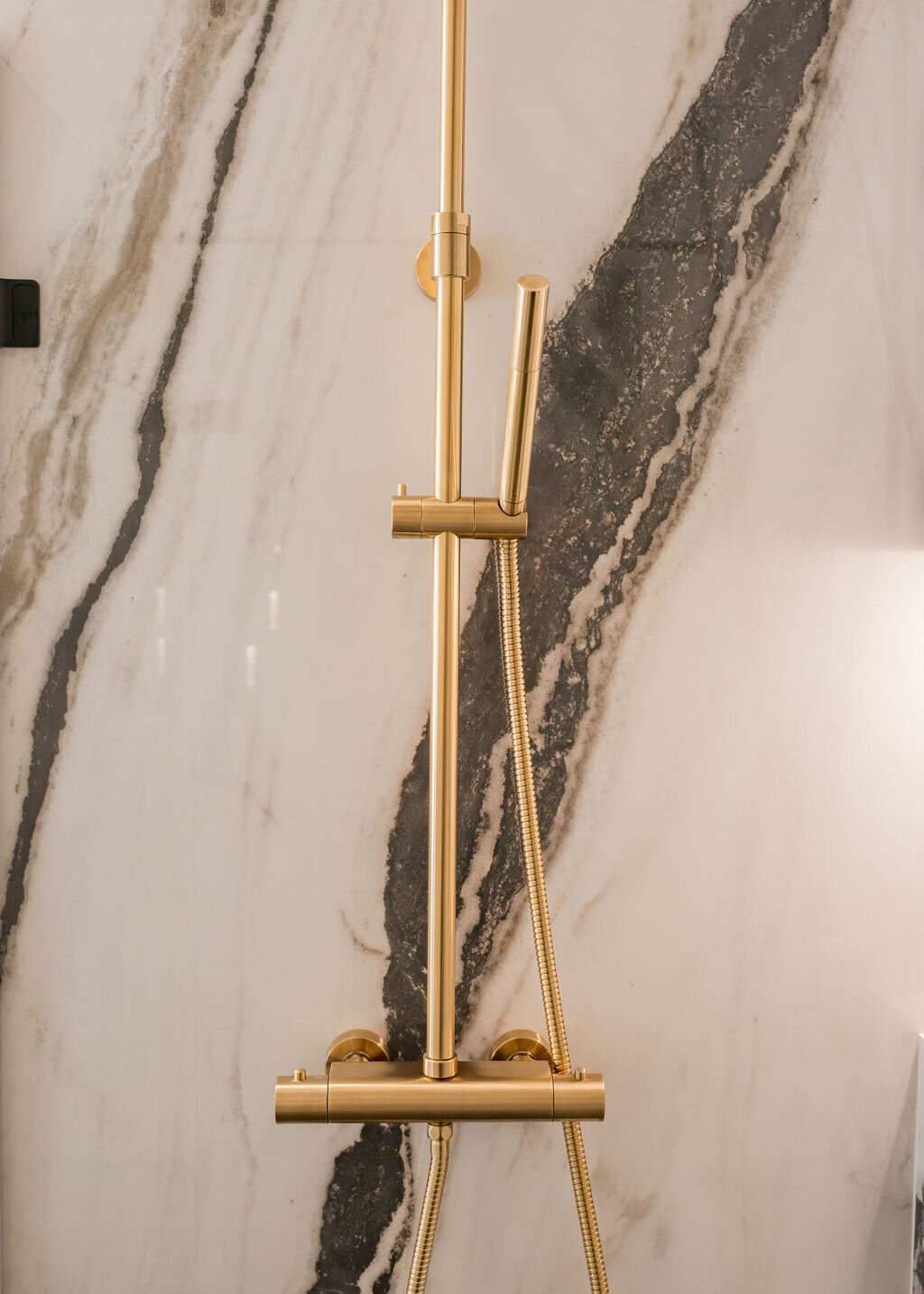 A modern shower with marble walls featuring black veining. The shower hardware is a chic gold.