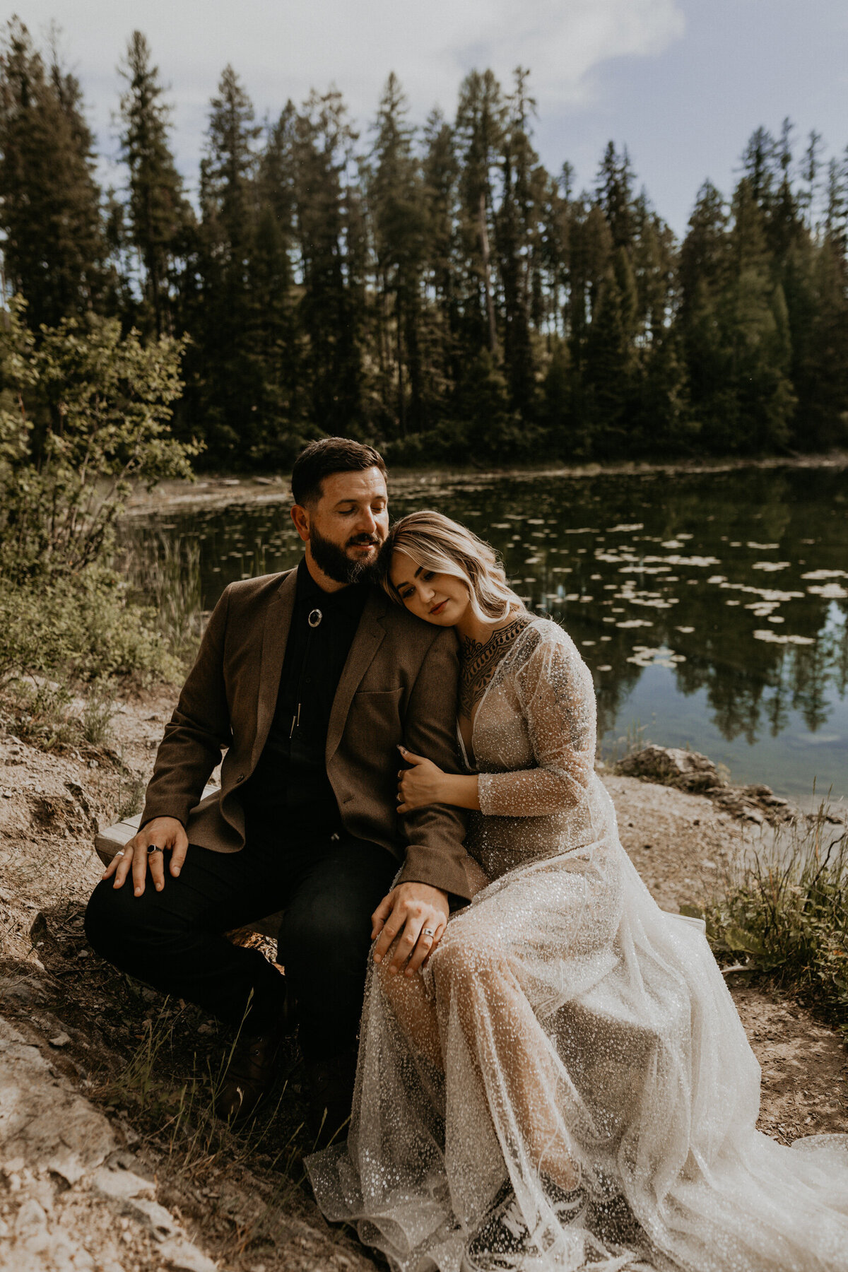 bride and groom sitting in front of a lake together