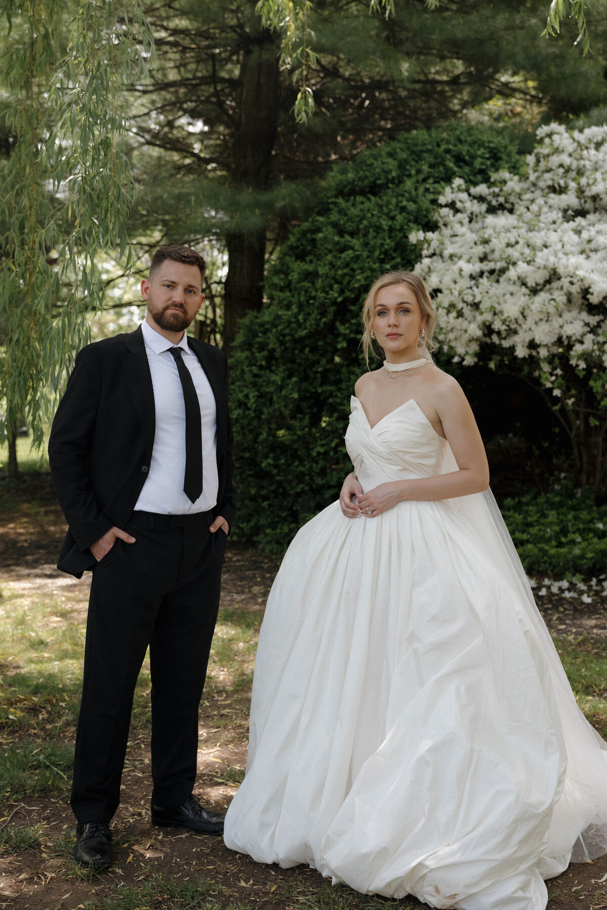 Editorial-style portrait of bride and groom captured elegantly in an intimate garden setting, emphasizing candid sophistication.