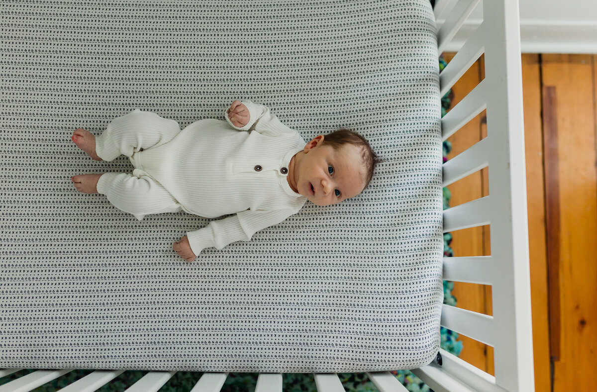 Infant photographer capturing a newborn baby sleeping in crib