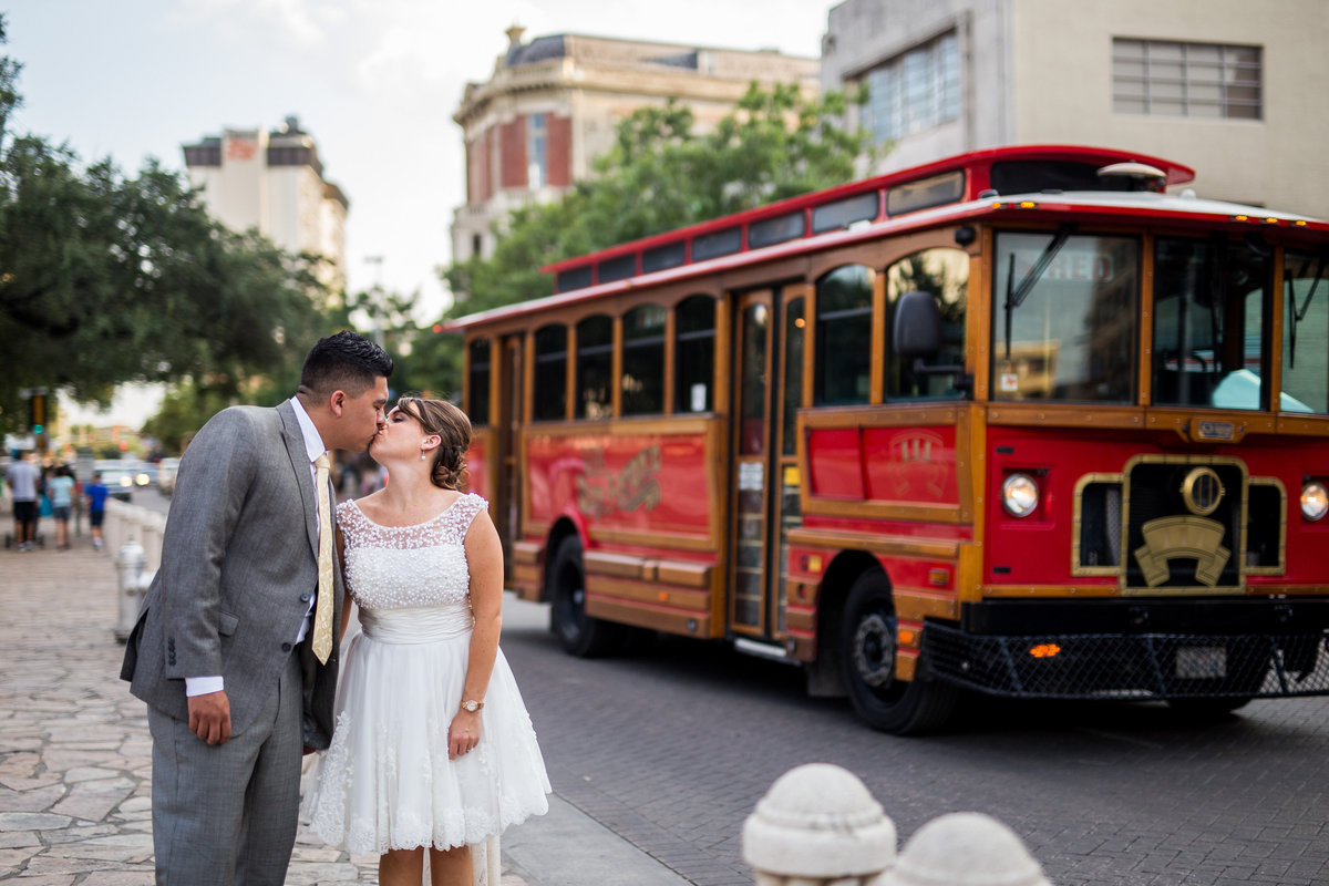 bride and groom kissing in front of red trolley in downtown San Antonio by the Alamo