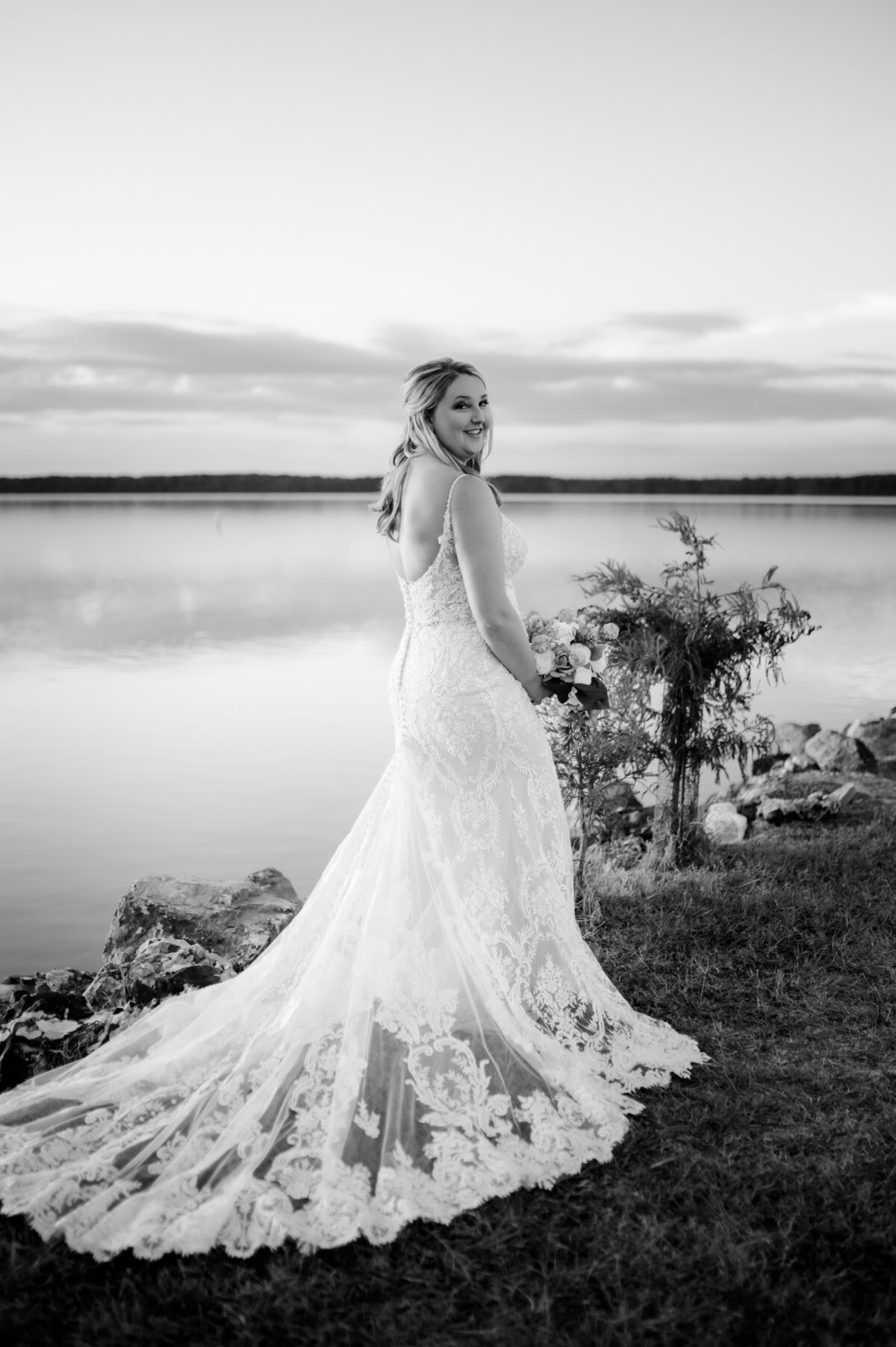 black and white bridal portrait with brides lace gown spread across the lawn in front of a lake in little rock arkansas