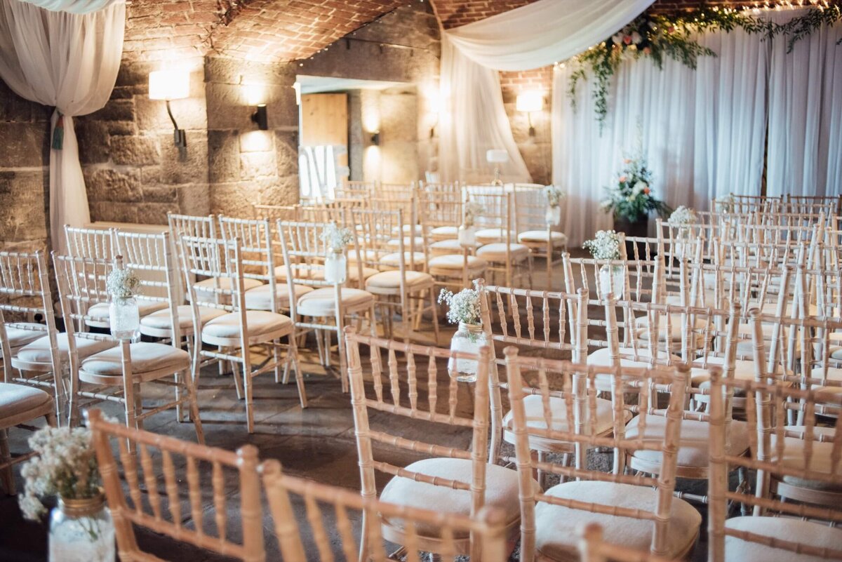 A room filled with lots of white chairs ready for the wedding ceremony