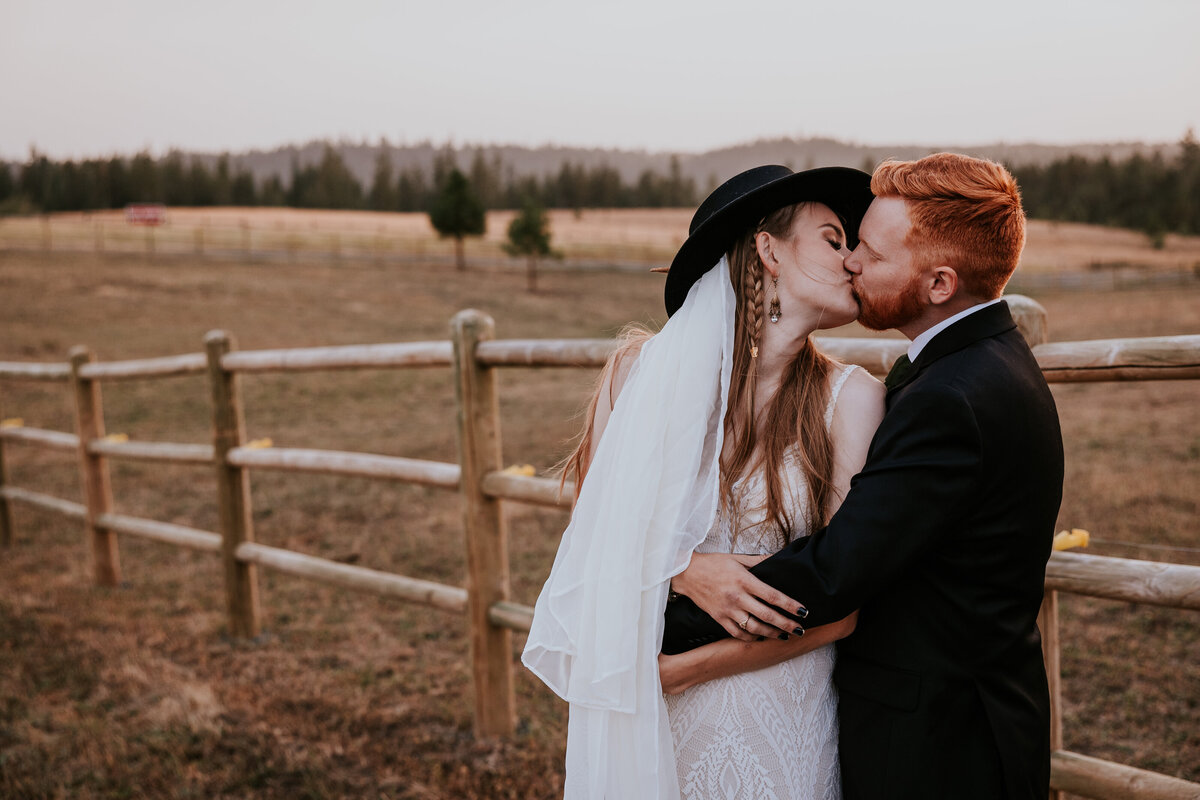 Bride and groom kiss in the middle of a farm field.