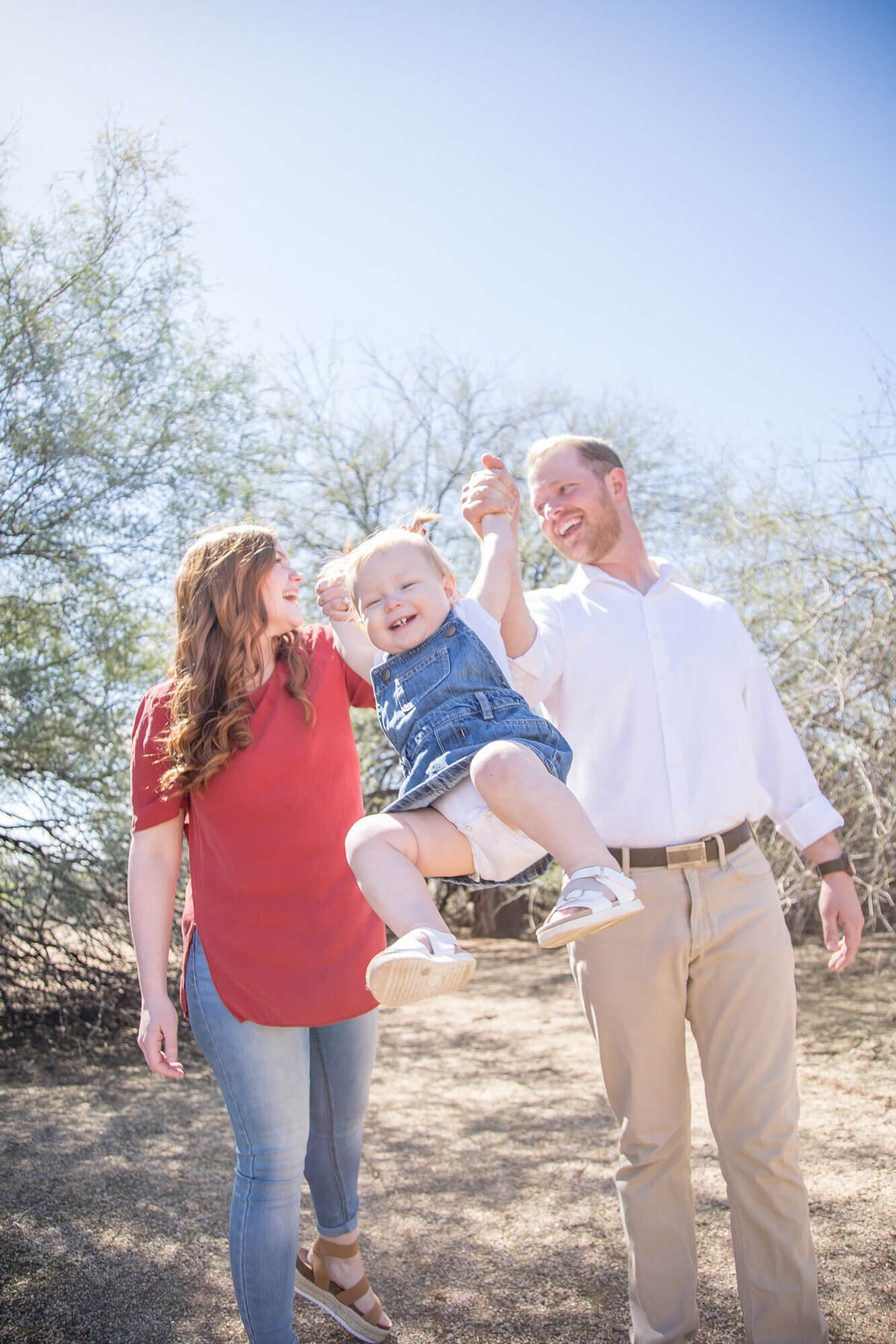 Couple laughing and swinging Joyful toddler daughter  in denim dress