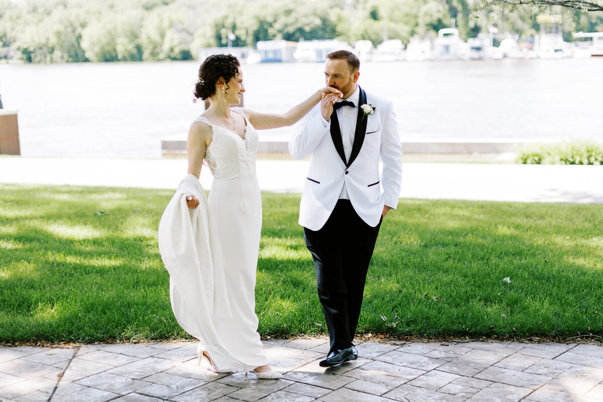 groom and bride walking along the river while he kisses her hand with a smile