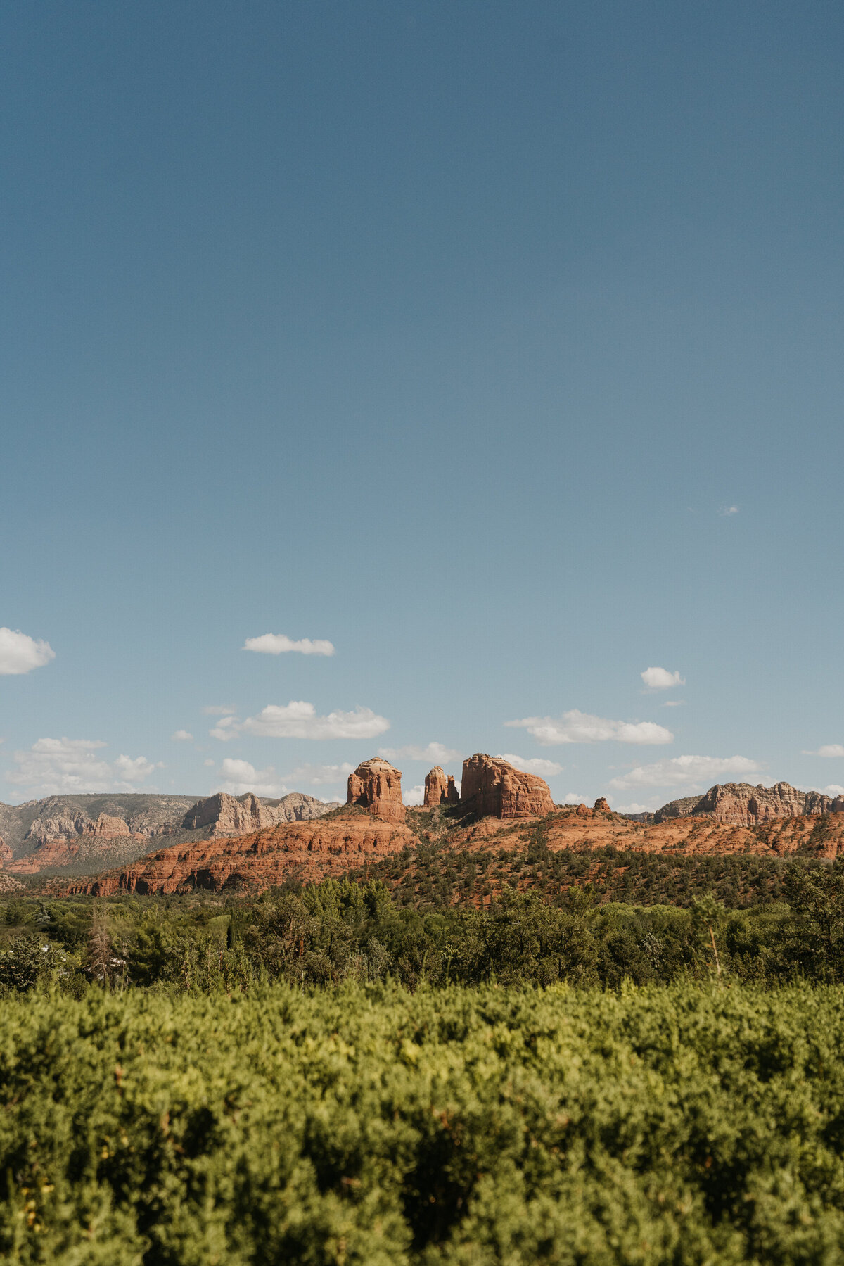 View of a red rock formation with green trees in front of it 