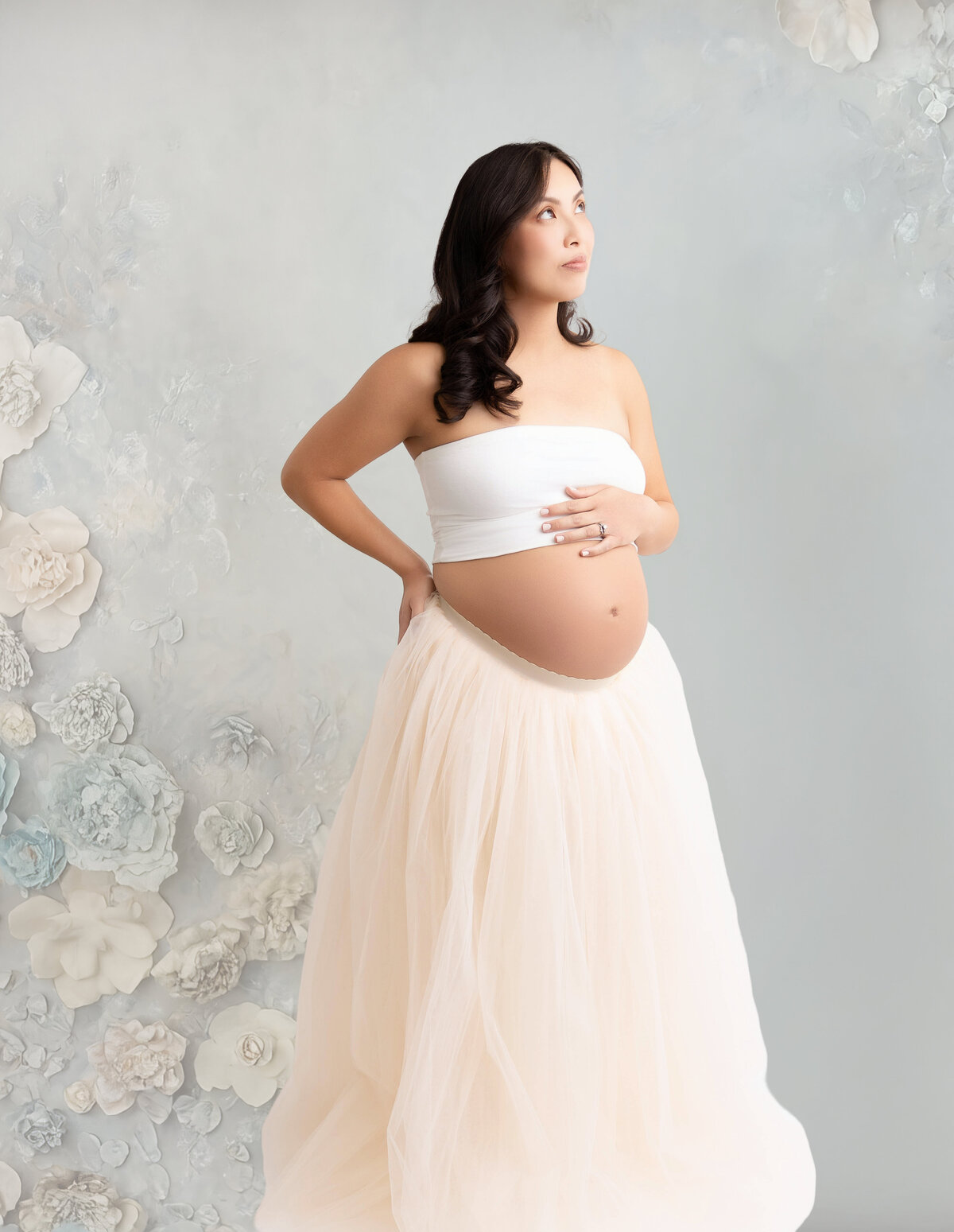 Pregnant mom wearing a white tube top and light pink skirt posing against a light mint green-flowered backdrop.