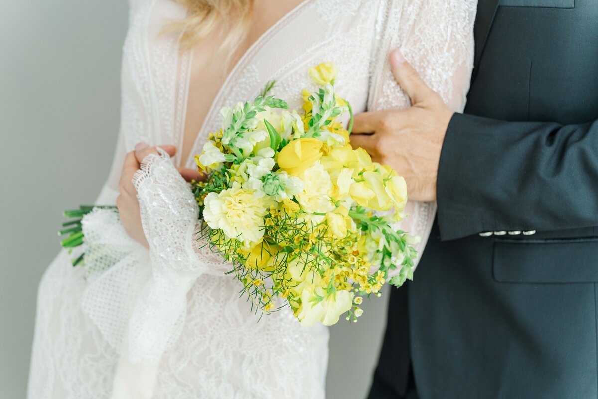 detail of a ywllow flowers wedding bouquete, holded by the bride, while the groom is behind her