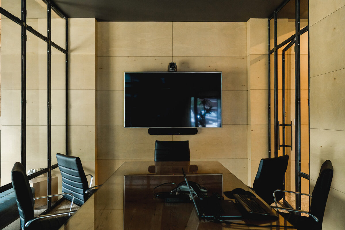 conference room with TV on plywood wall surrounded by black mullion storefront glass walls