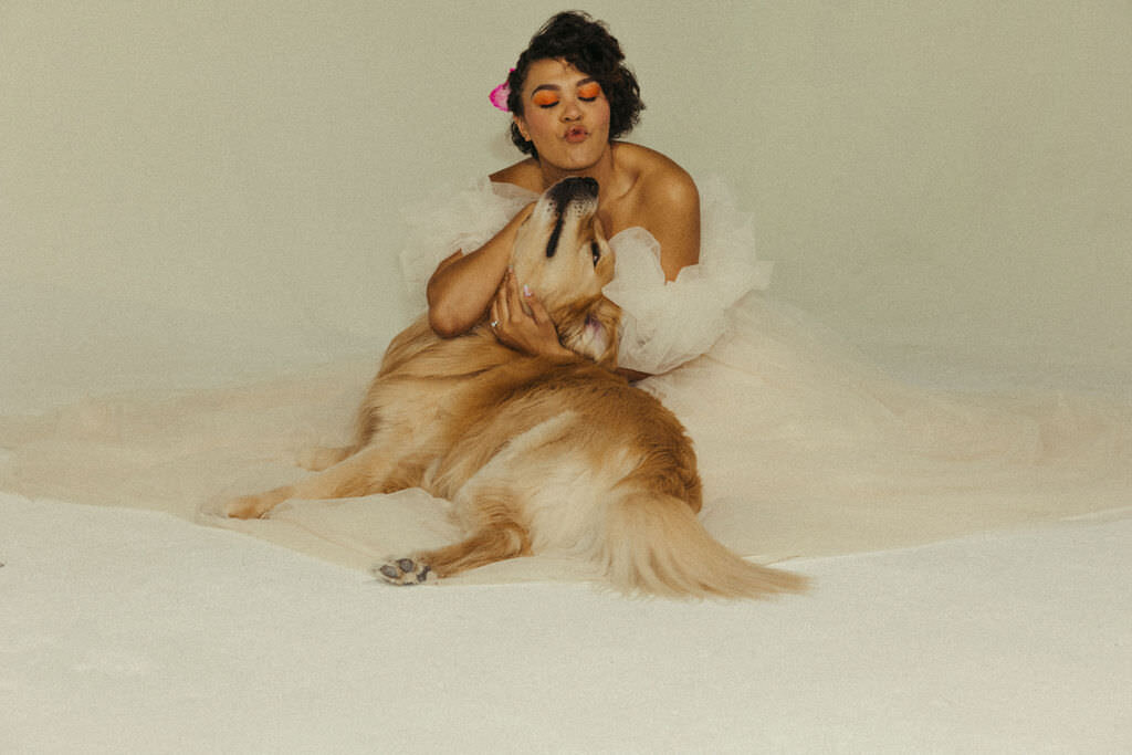 A person in a wedding dress sitting on the floor with a dog.