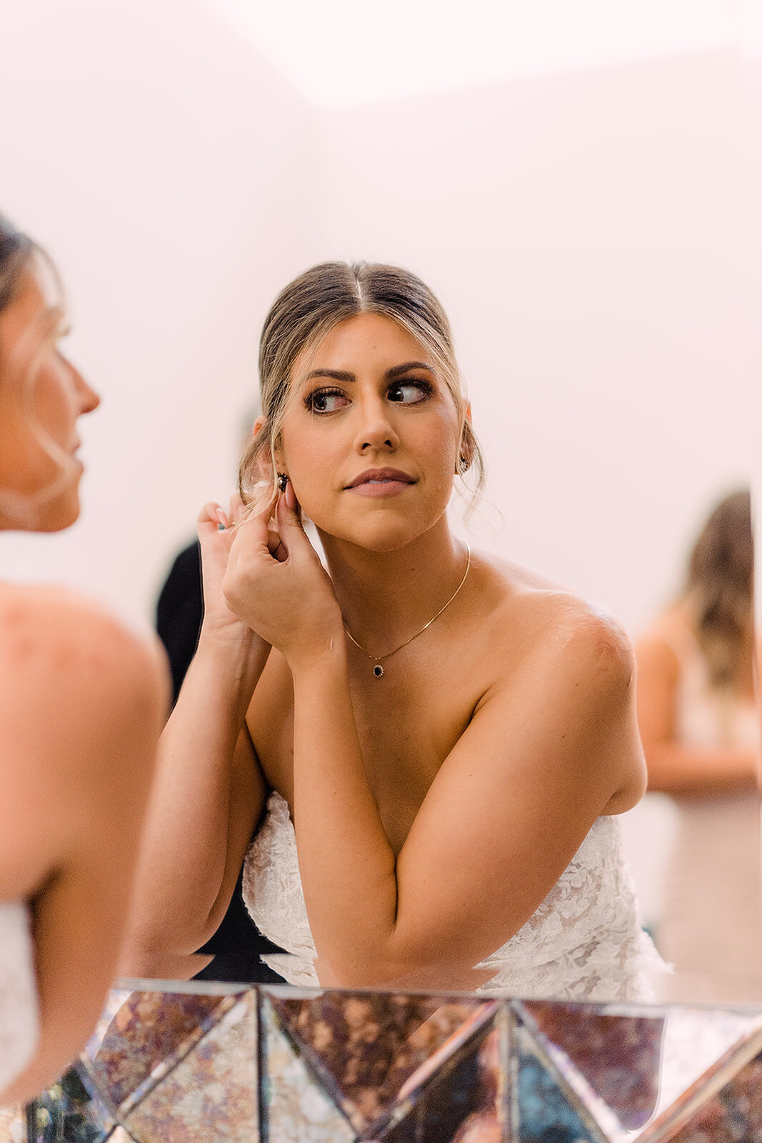 Bride adjusts her earring, looking thoughtfully into a mirror as she prepares for her big day.