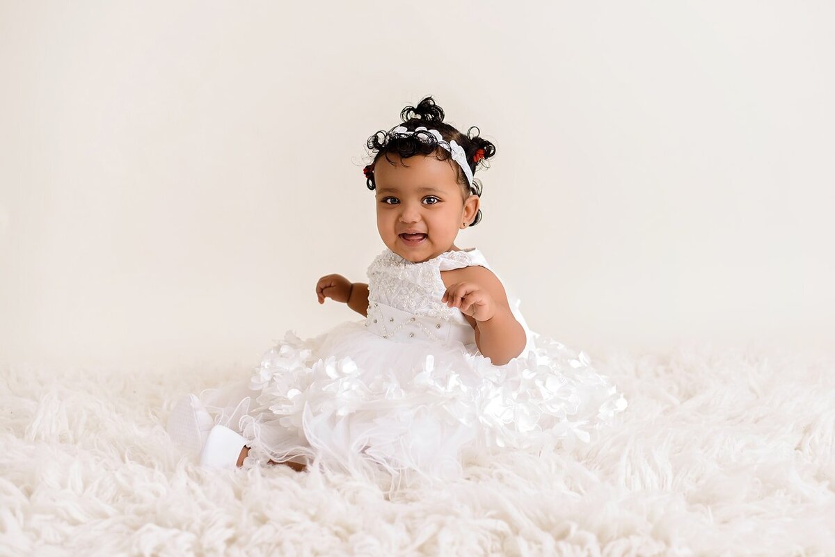 One year old girl smiling in all white dress.