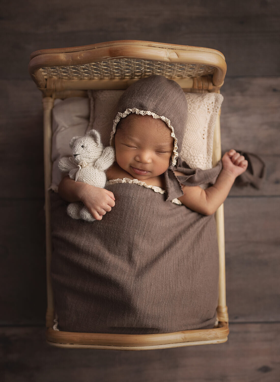 A newborn baby sleeps in a small wicker bed holding a stuffed bear by a New Orleans Newborn Photographer