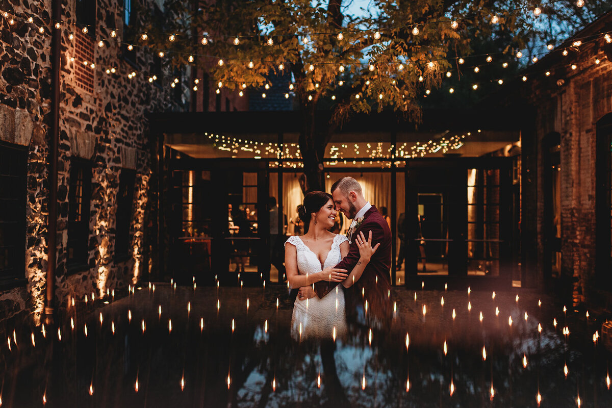 Outdoor wedding pictures with bride and groom embracing each other while twinkle lights above them turn on for the nighttime wedding captured by Maryland wedding photographer