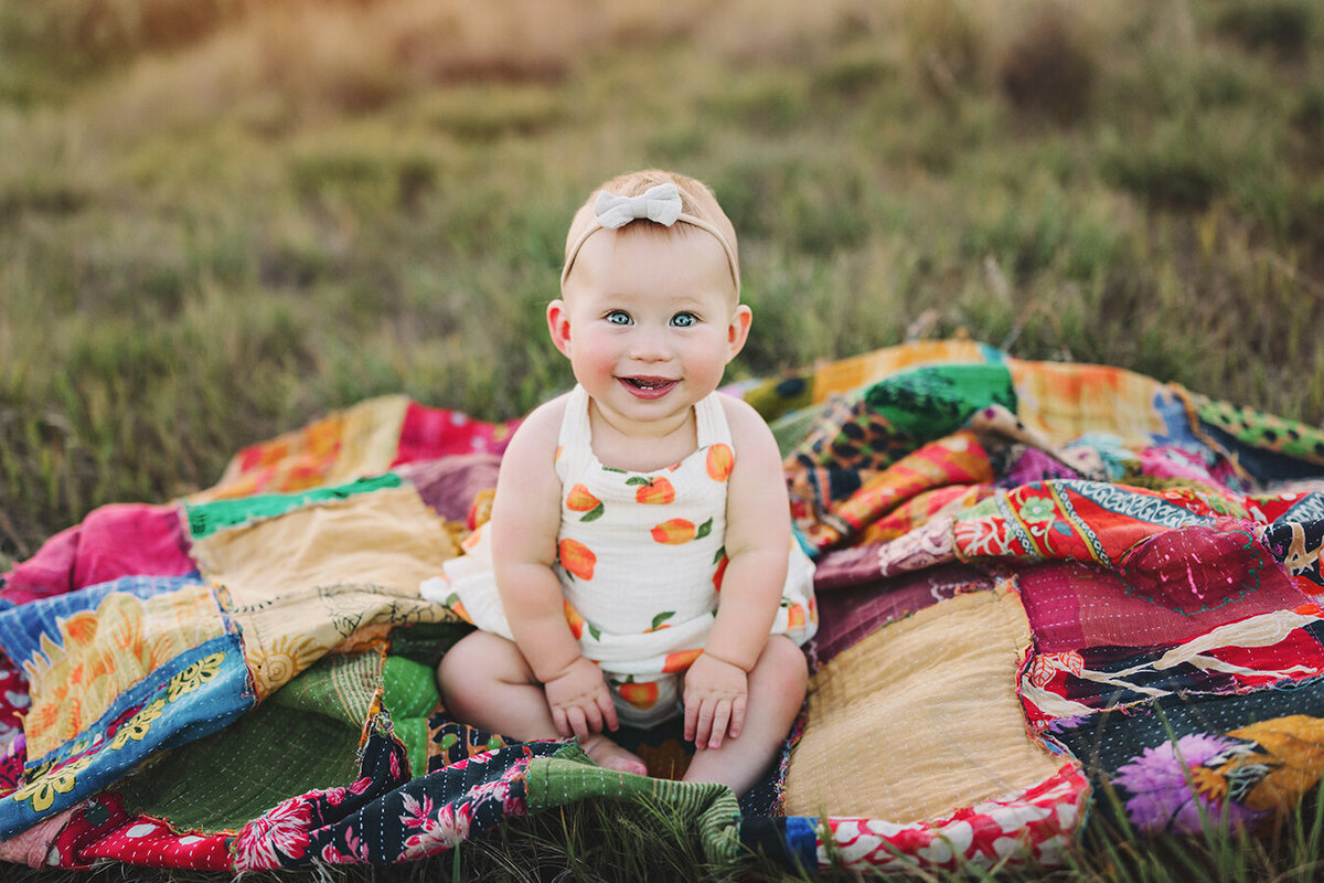Beautiful baby girl sitting on a colorful blanket smiling