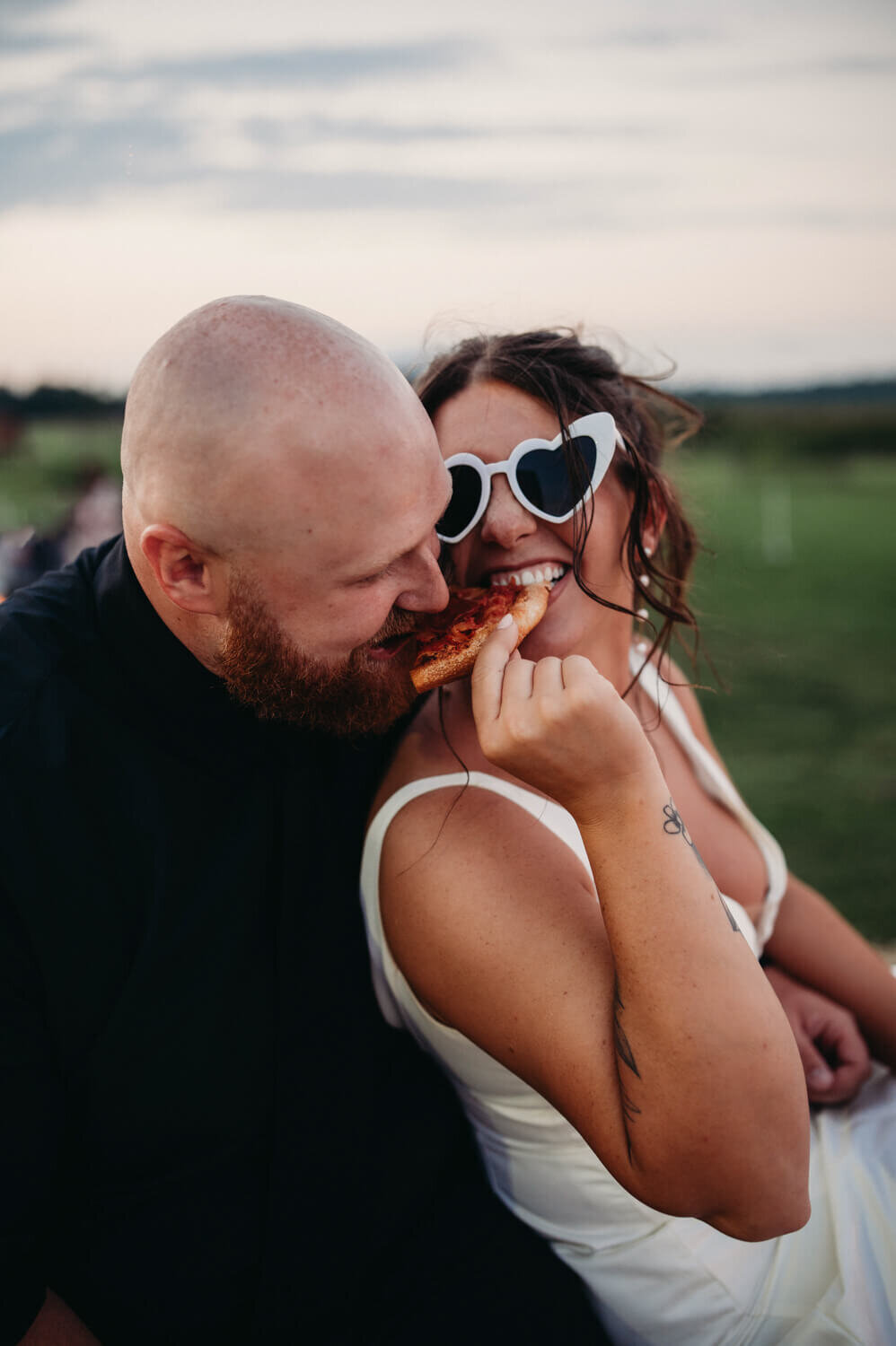 Laughing couple share a piece of pizza at sunset on their wedding day in Ohio.