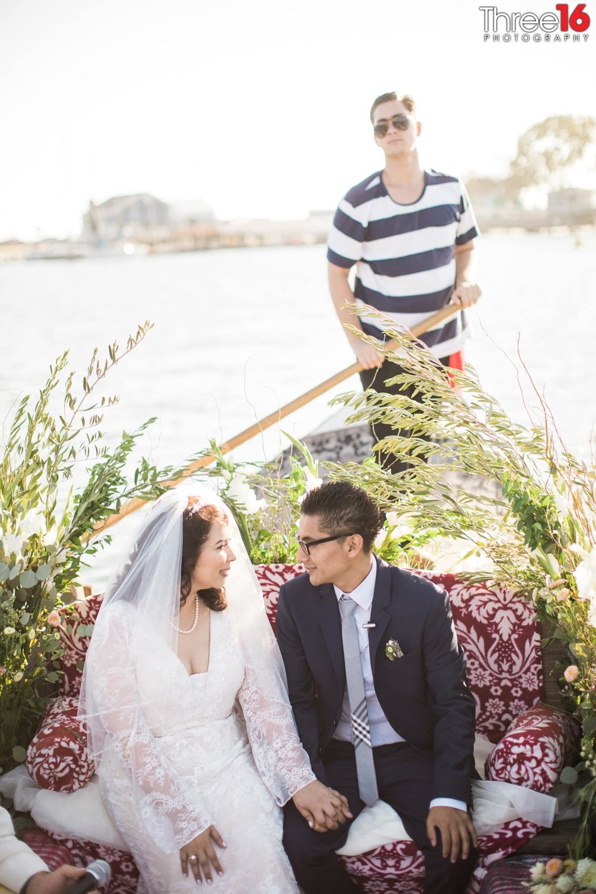 Bride and Groom sit holding hands and gazing at each other on a gondola ride with driver in the back