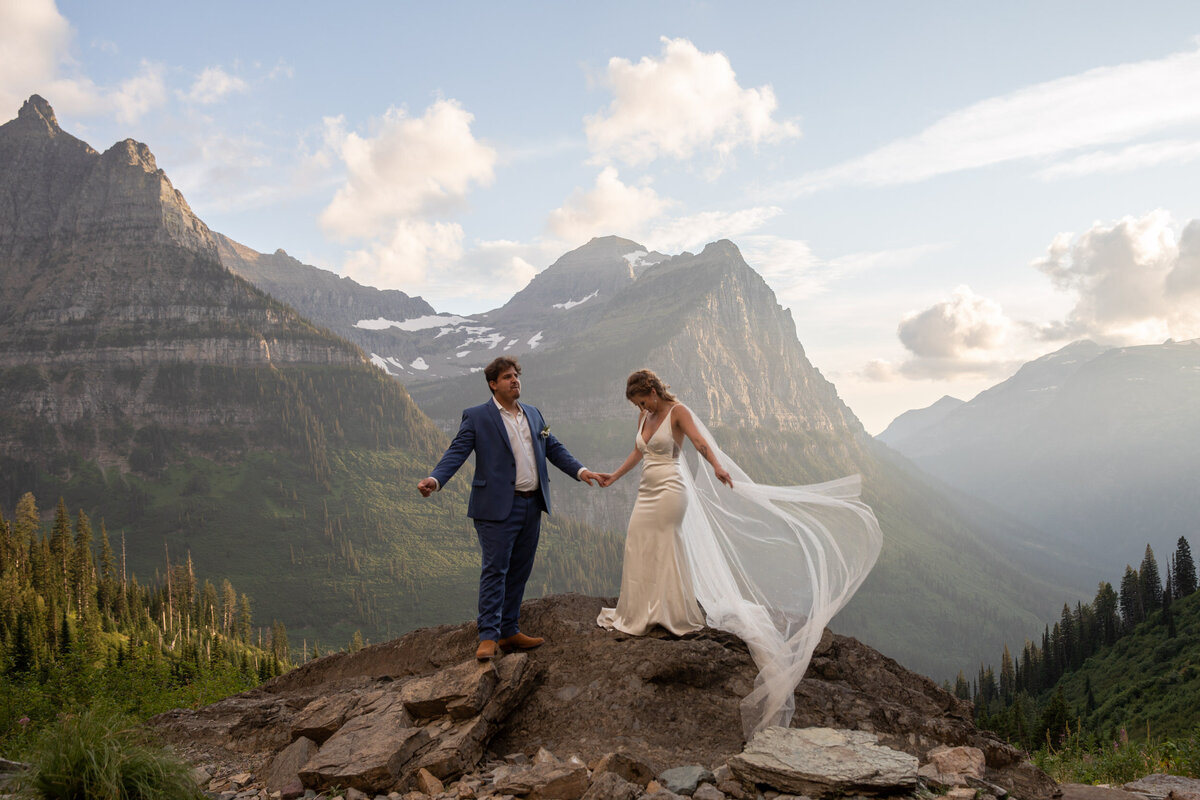 A bride and groom stand on a rock in Glacier National Park on their elopement day.