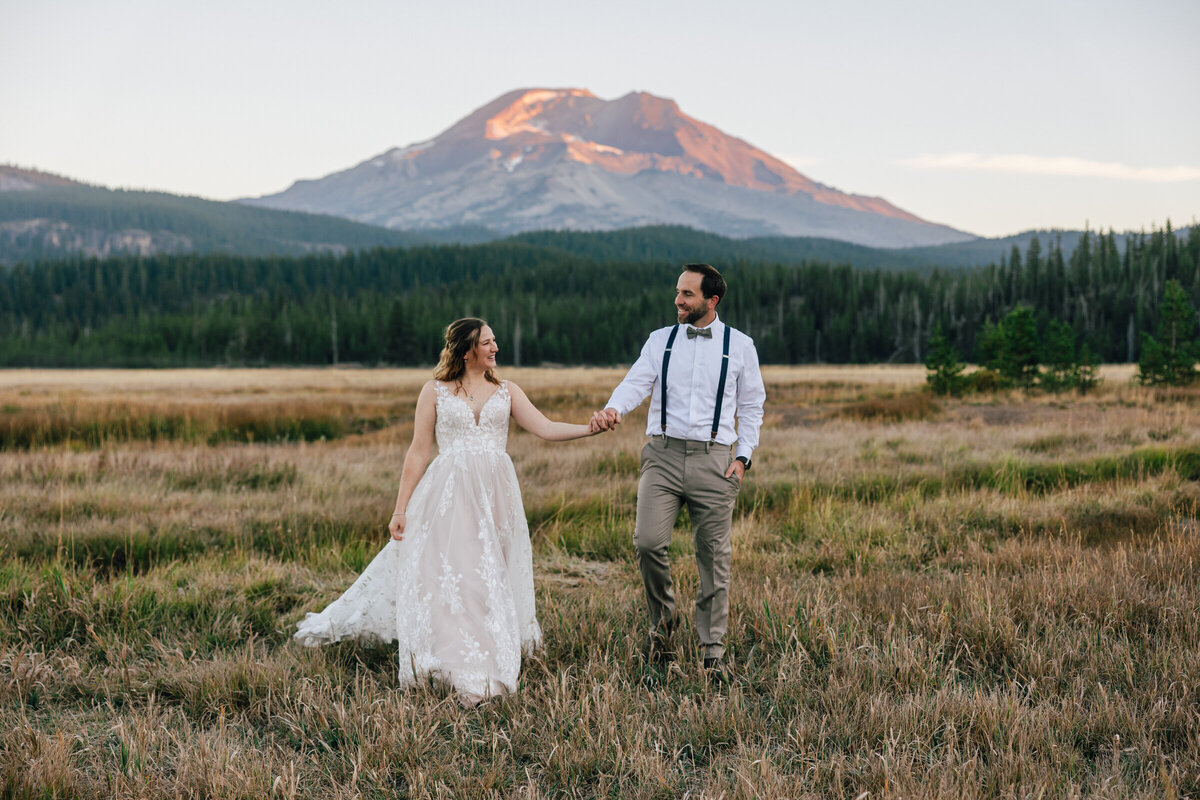 A bride and groom walk along a creek as the alpenglo lights up South Sister near Sparks Lake for their Bend Oregon elopement.