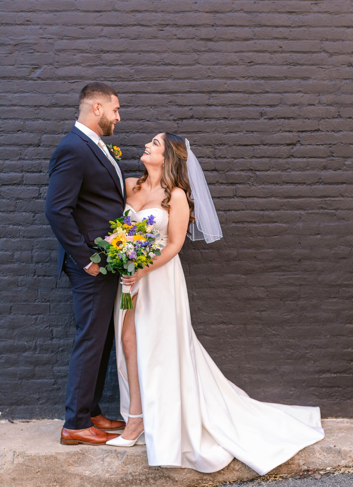 Bride and Groom looking at each other in front of black brick wall outside The Refinery at 120 in Culpeper, Virginia.