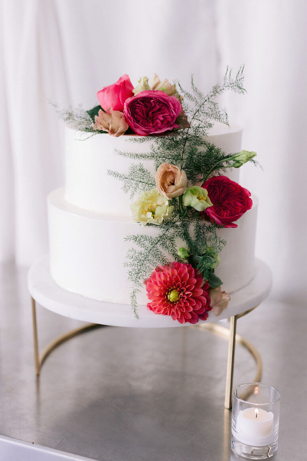 A two-tiered white wedding cake with beautiful red flower toppers. Image by Jenny Fu Studio