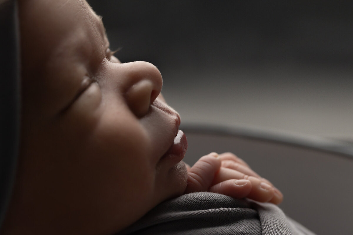 Close-up of a newborn's serene face and tiny hand, captured by Fort Worth newborn photographer in soft natural light.