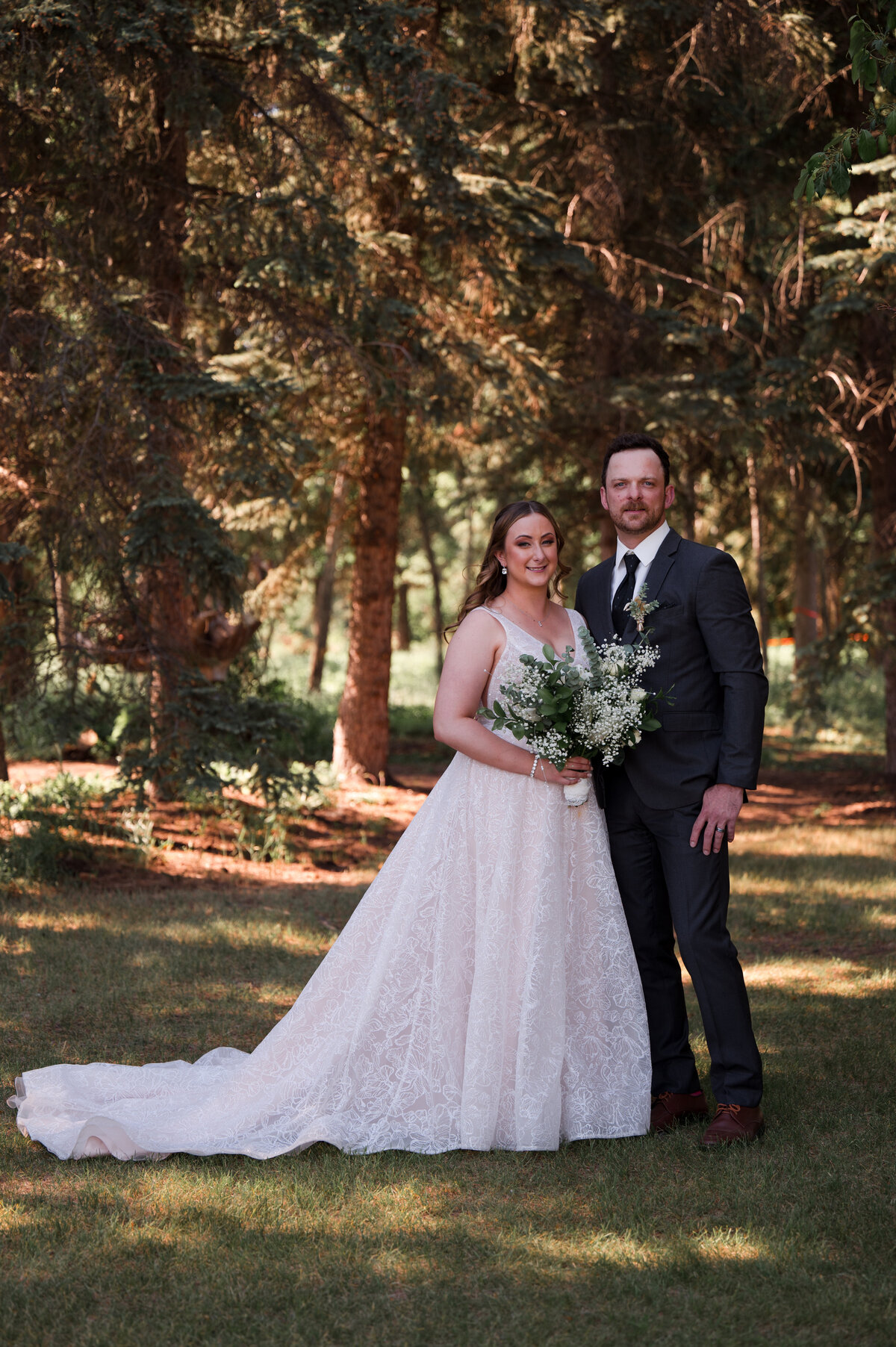 bride and groom stand in a forest with golden light filtering through 