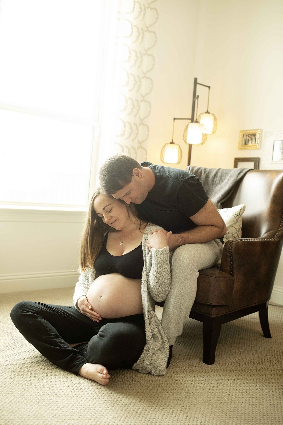 A heartwarming maternity portrait of mom and dad in the bedroom, sharing a loving glance as mom cradles her belly and dad lovingly wraps his arm around her, captured by Chunky Monkey Photography.