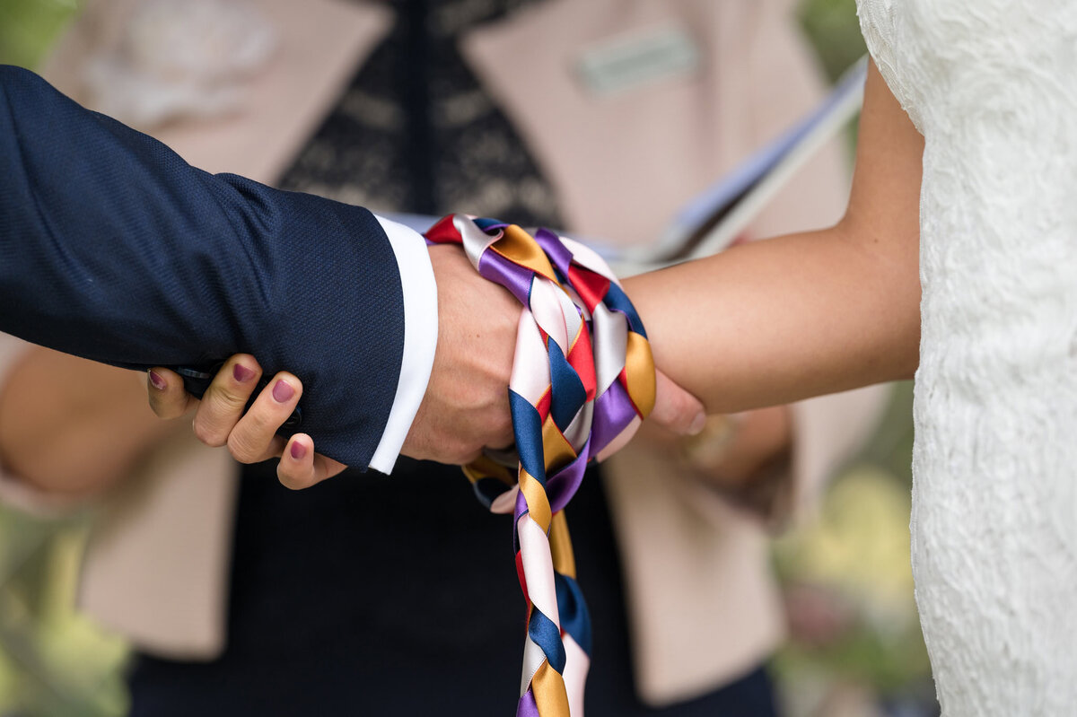 Close up photo showing a couple's hands bound with beautiful knotted ribbons during their handfasting