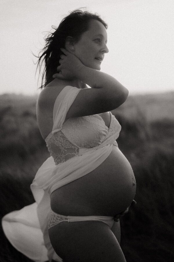 Portrait en noir et blanc d'une femme enceinte, ventre apparent, regard tourné vers l'horizon. Séance photo grossesse artistique par Kamescop.
