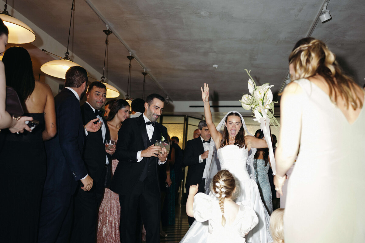 Newlyweds entering reception surrounded by cheering guests

