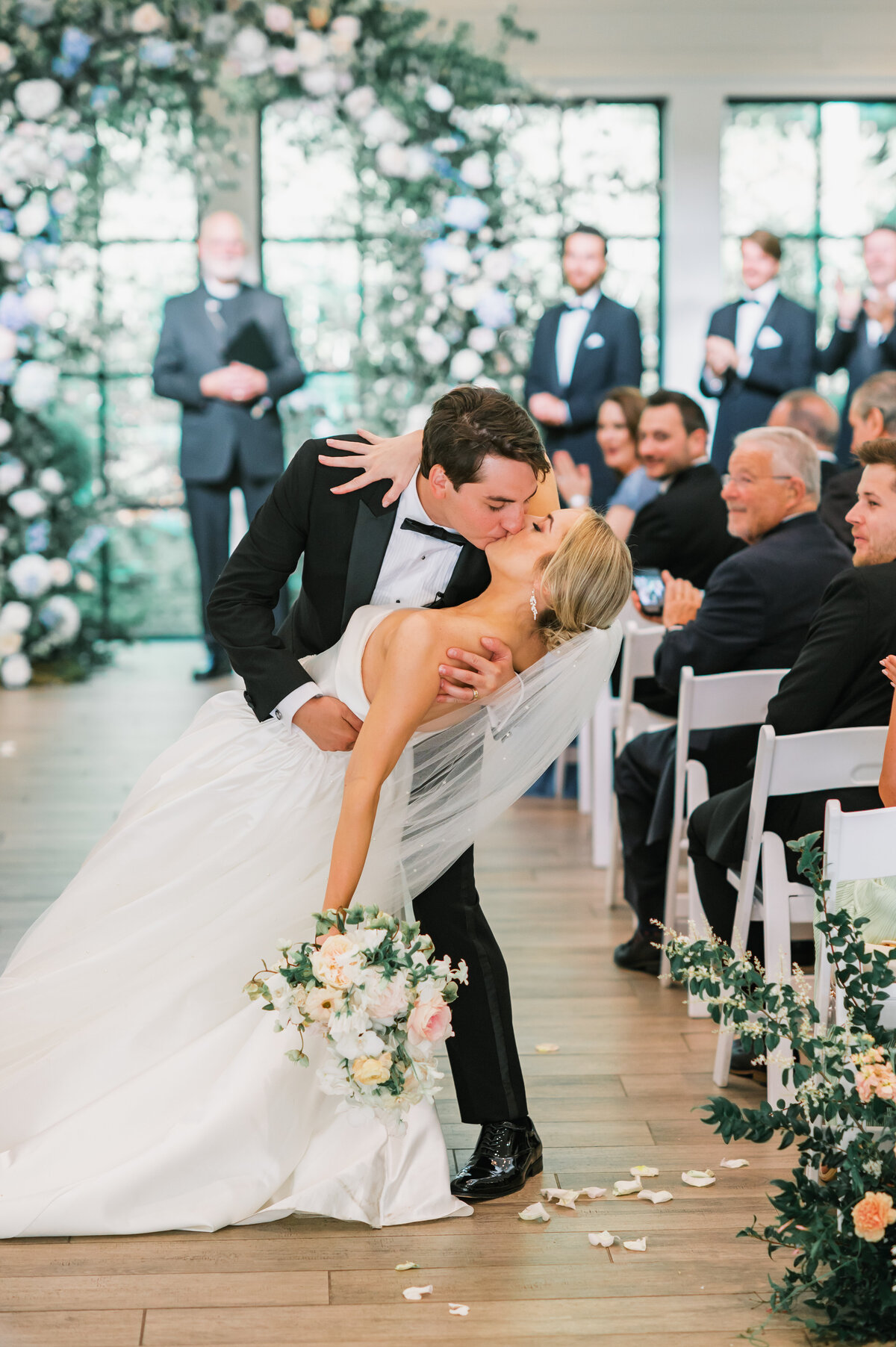 Groom dips and kisses the bride during their wedding ceremony exit, surrounded by floral aisle arrangements and cheering guests at Old Edwards Inn in Highlands, North Carolina.