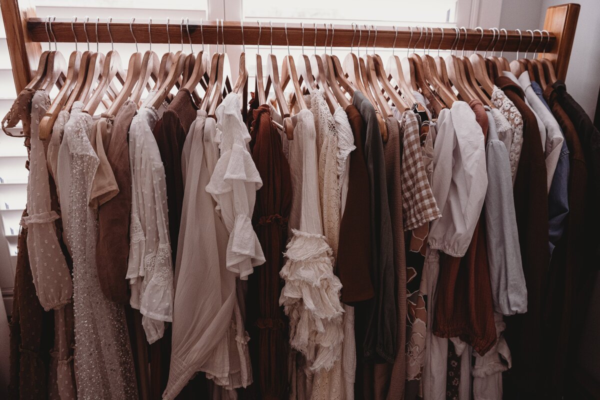 A wooden clothing rack with various hanging garments, including dresses, blouses, and shirts in neutral and earth tones—perfect for those Wollongong motherhood sessions or South Coast newborn photography shoots.