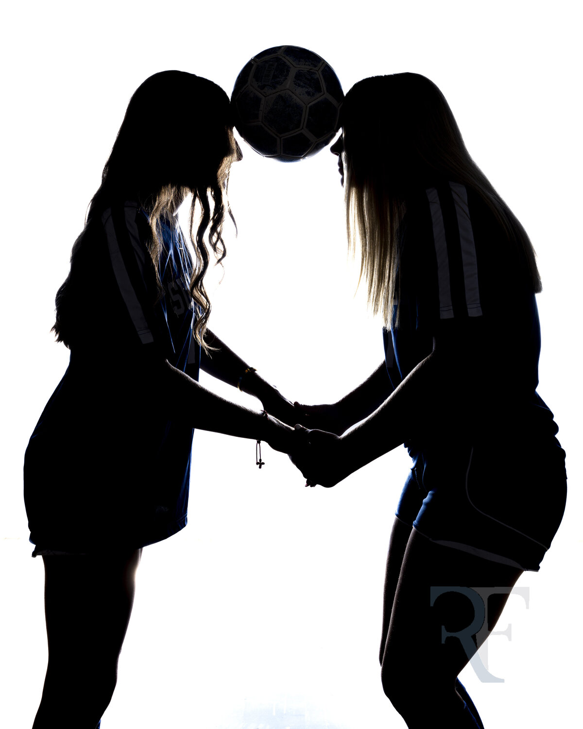 Photographer in Avon | Rob Faber Photography | Silhouette of two soccer players pressing foreheads with a soccer ball between them, holding hands for balance.