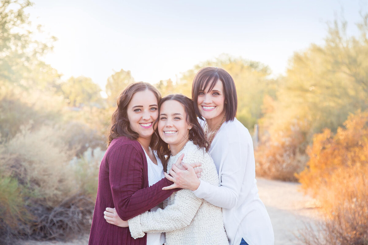 three brown haired women hugging on a desert park path