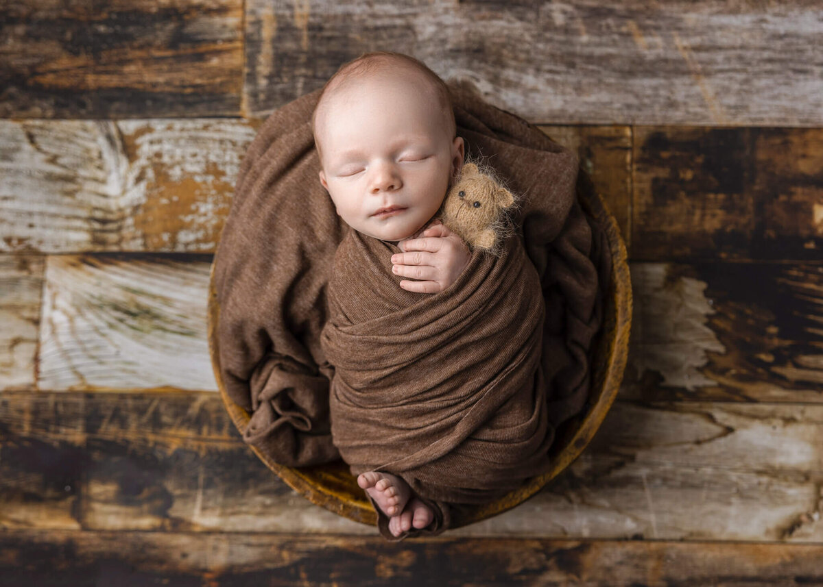 newborn baby asleep in a wooden bowl  holding a tiny teddy bear