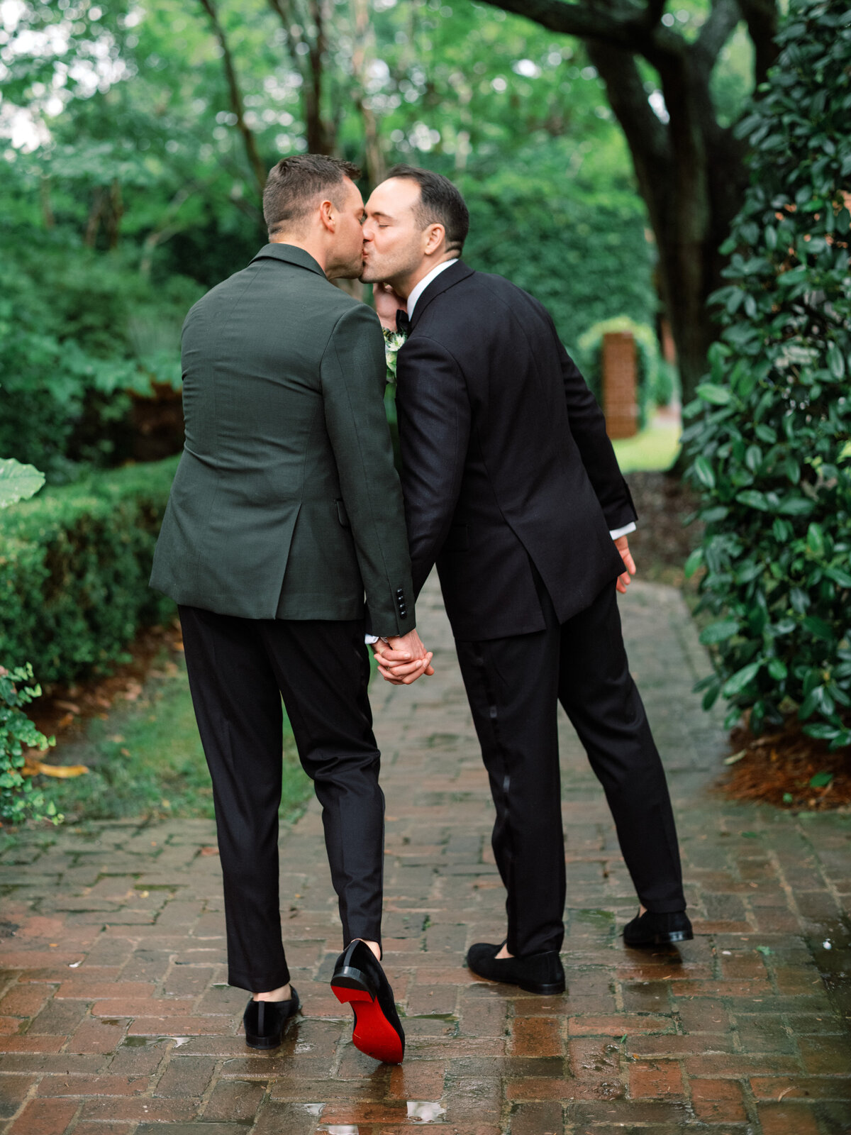 A romantic moment captured as a couple shares a loving kiss while holding hands, blissfully enjoying their special day amidst a beautiful natural setting in an elegant portrayal.