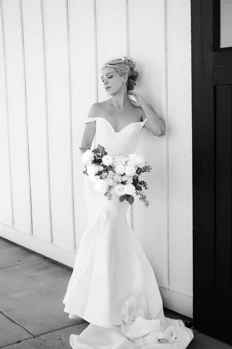 black and white bridal portrait leaning against farmhouse with bouquet