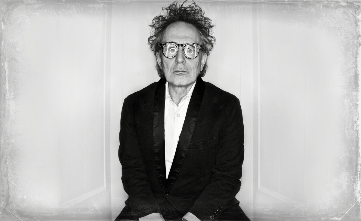 Classical music photo black and white Marc Jordan wearing black suit coat eye glasses with circle light reflections against white backdrop