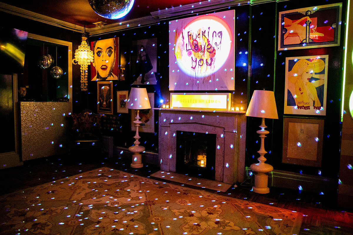 Interior lounge at Norwood in New York featuring pop art, disco lights, and a fireplace with eclectic decor.