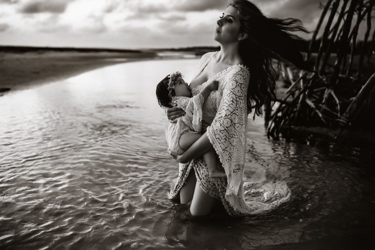 a mom breastfeeding her 1 year old while sitting in the water at the beach
