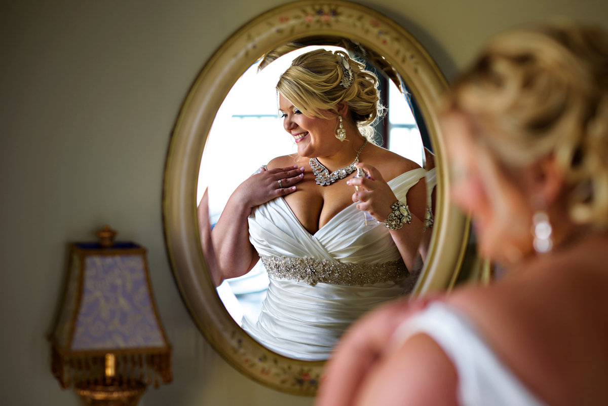 A beautiful bride applies her perfume in the mirror before her ceremony.