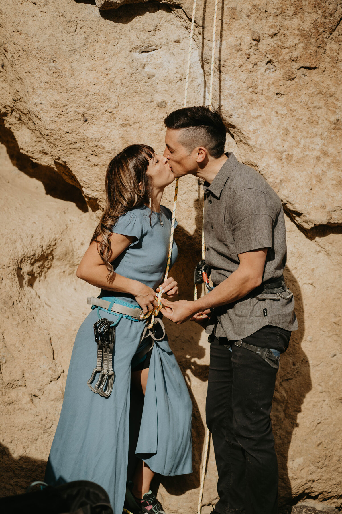 Couple kissing while getting rock climbing gear ready for rock climbing engagement photos