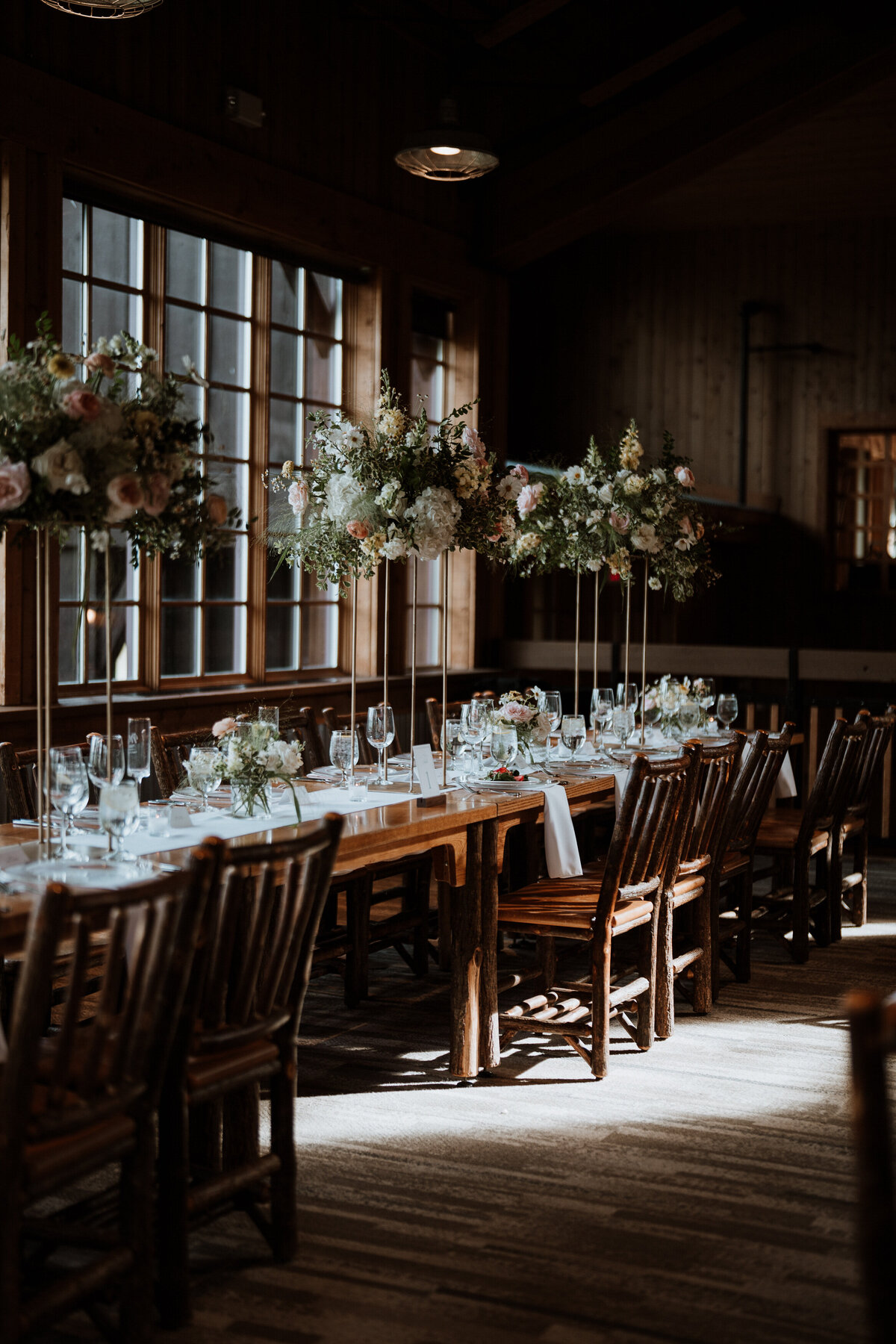 Reception tables with tall floral arrangements and wood accents inside Breckenridge wedding venue, Ten Mile Station.