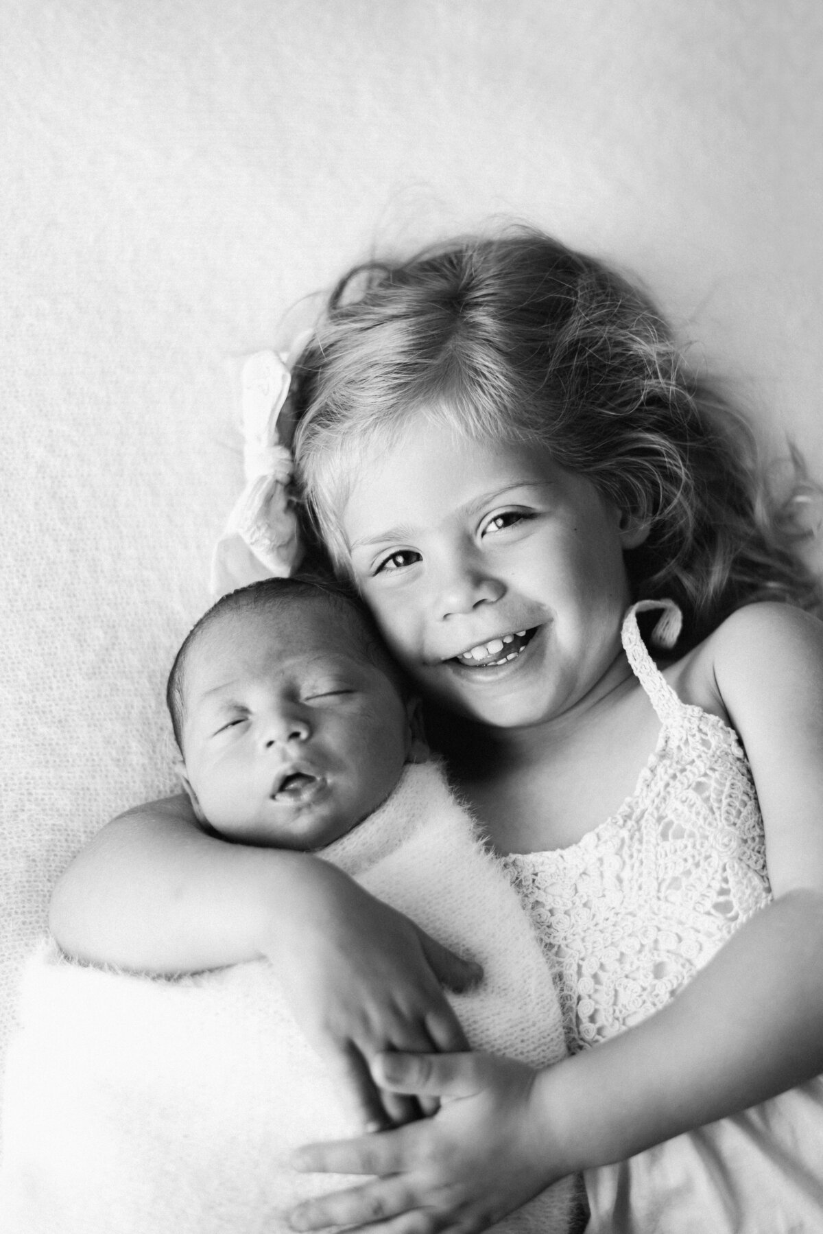 Big sister holding her newborn brother and smiling at newborn photoshoot in Billingshurst