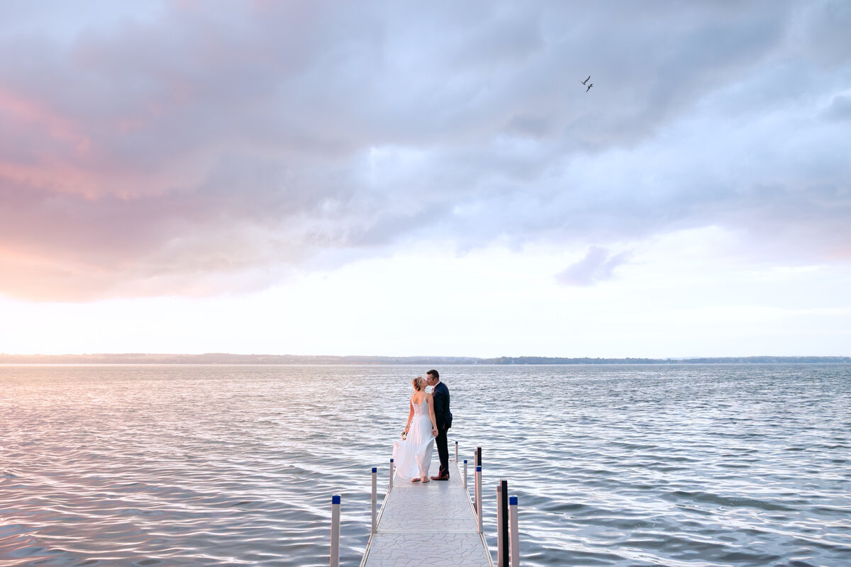 Bride and groom kiss on a dock at their backyard lake wedding in Minnesota.