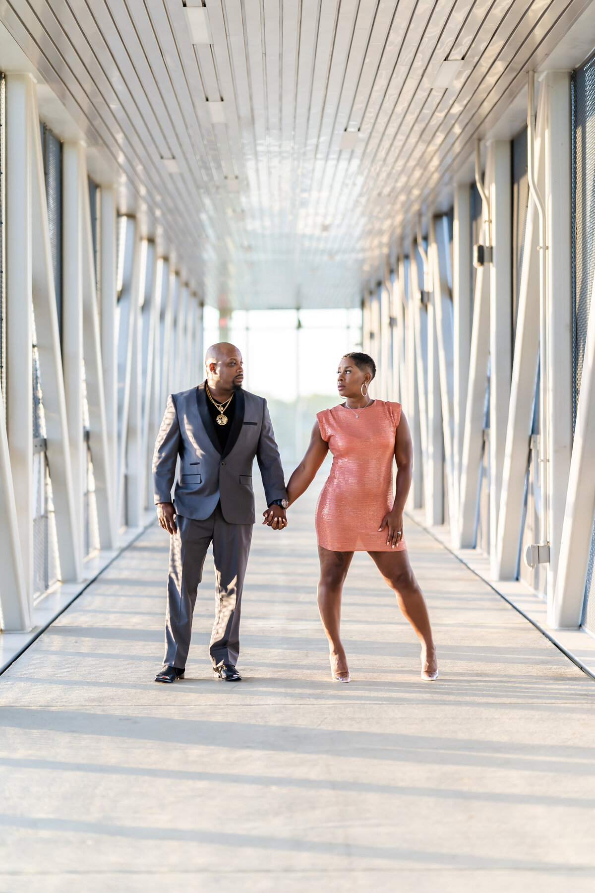 Wedding anniversary photoshoot couple on bridge man wearing grey suit, woman wearing coral sequin dress